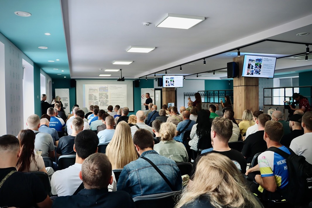 Аудиторія слухає презентацію в конференц-залі, на екрані — слайди з інформацією.