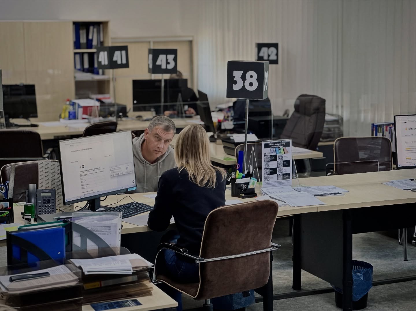 Жінка сидить за робочим місцем і спілкується з чоловіком.