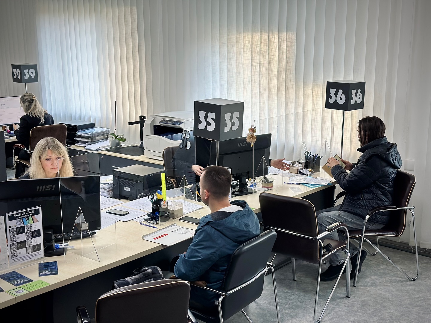 Двоє людей працюють за комп'ютером, а двоє людей сидять навпроти.