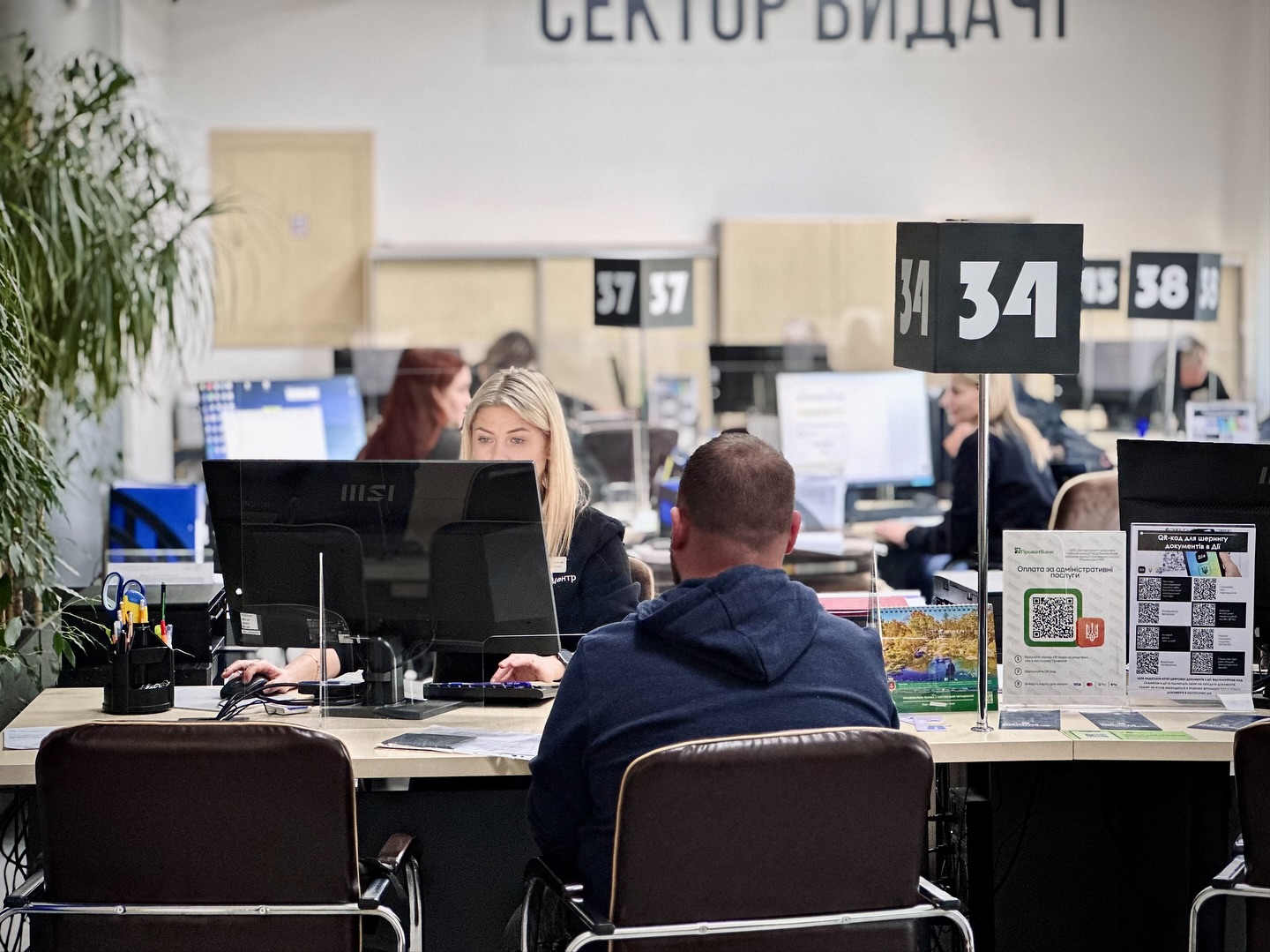 Жінка зі світлим волоссям працює за комп'ютером, чоловік сидить навпроти