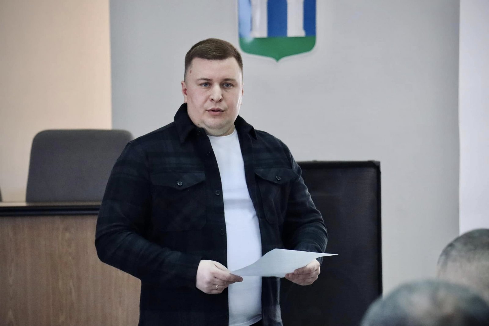 Чоловік у темній сорочці тримає папір, стоїть перед аудиторією