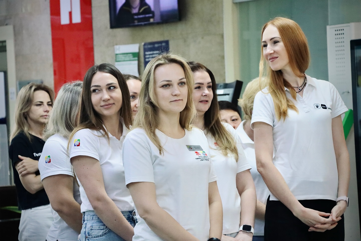 Група співробітниць у білих поло з логотипом ЦНАП стоять у ряд, слухають виступ.