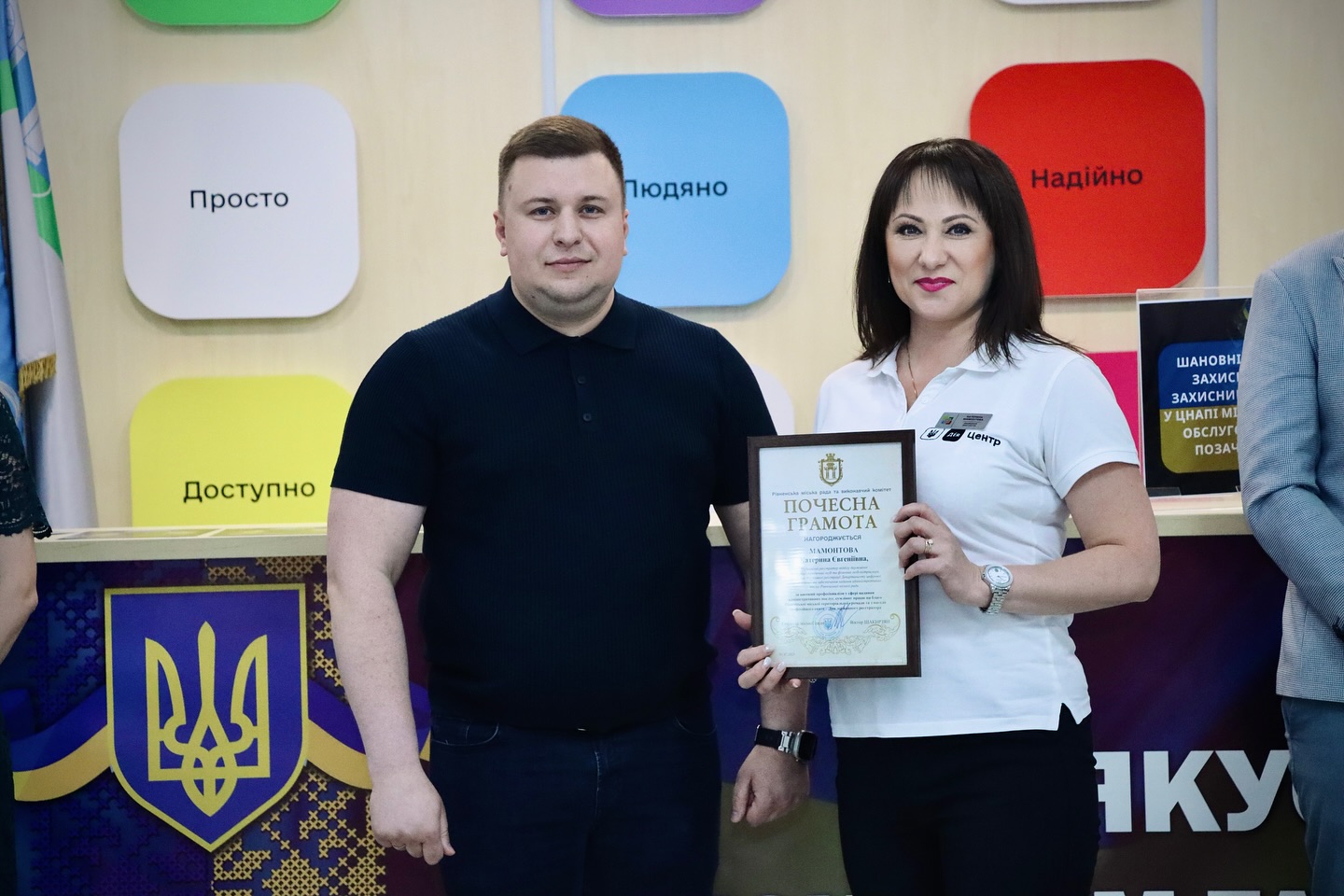 Чоловік і жінка стоять у приміщенні ЦНАП, тримають почесну грамоту, дивляться в камеру.