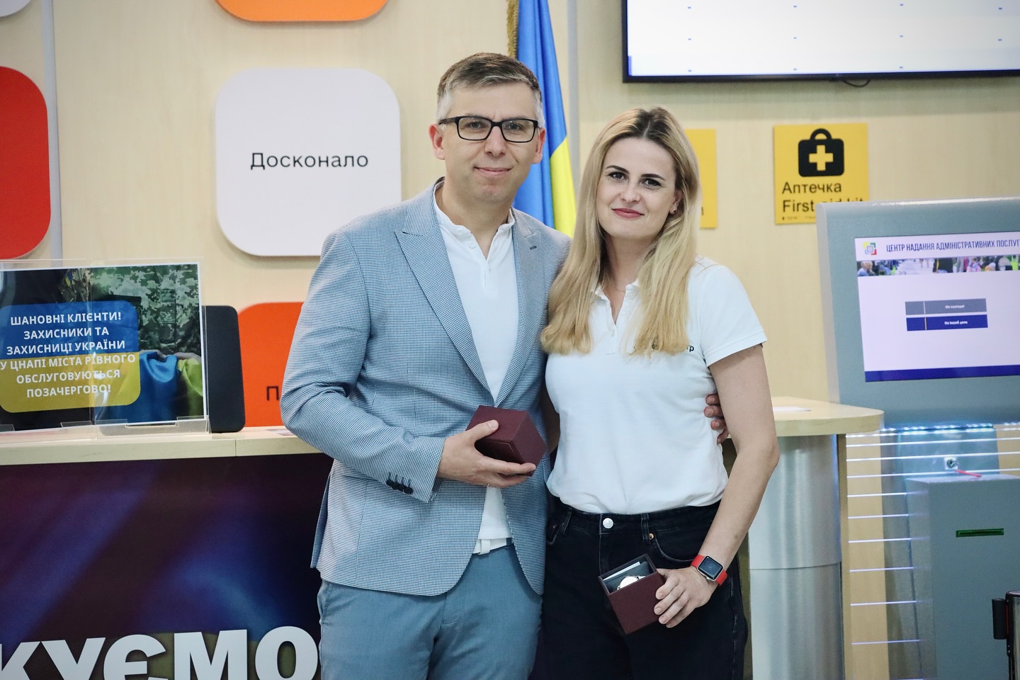 Чоловік і жінка стоять разом у приміщенні ЦНАП, тримають нагороди, усміхаються в камеру.