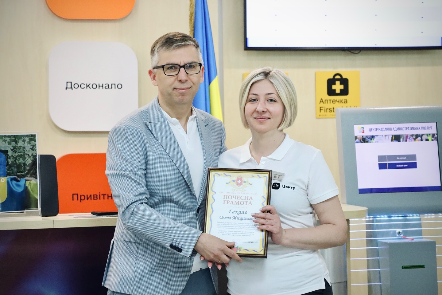 Чоловік і жінка з нагородою стоять разом біля стійки з написами «Досконало» і «Привітно».