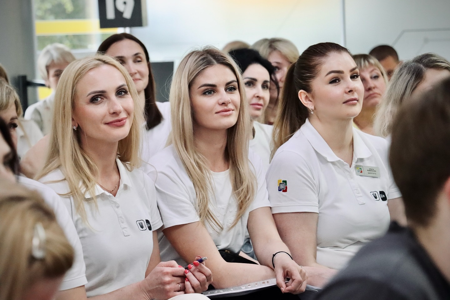 Багато жінок у білому одязі сидять у приміщенні.