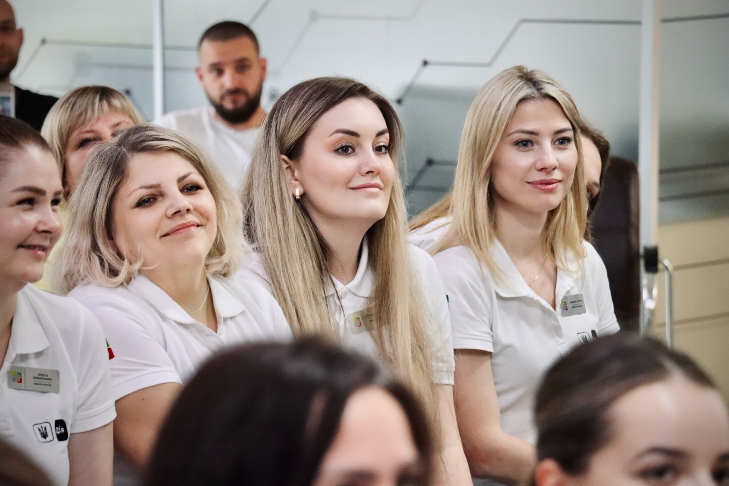 Жінки в уніформі з бейджами уважно слухають під час заходу.