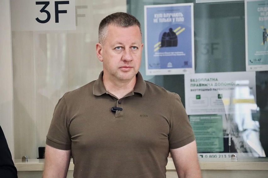 Чоловік в коричневому одязі стоїть у приміщенні.