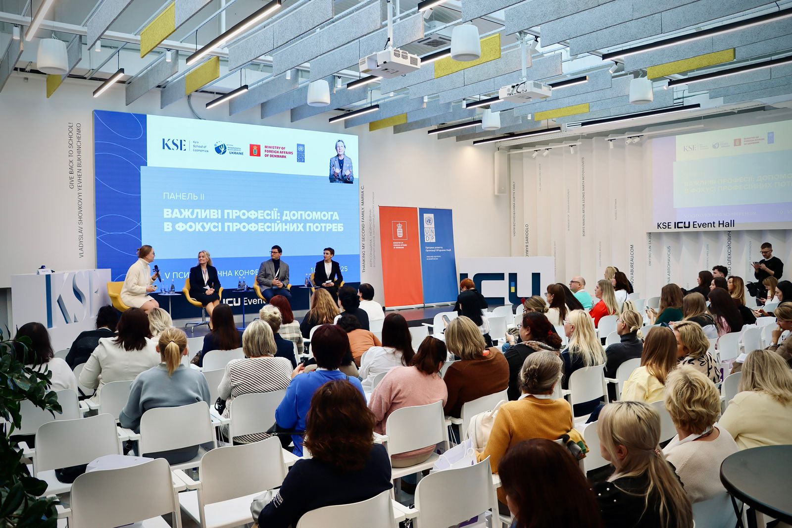 Група людей сидить  залі та слухають виступи спікерів.