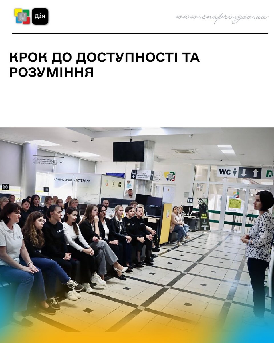 Група людей слухає виступ у приміщенні.