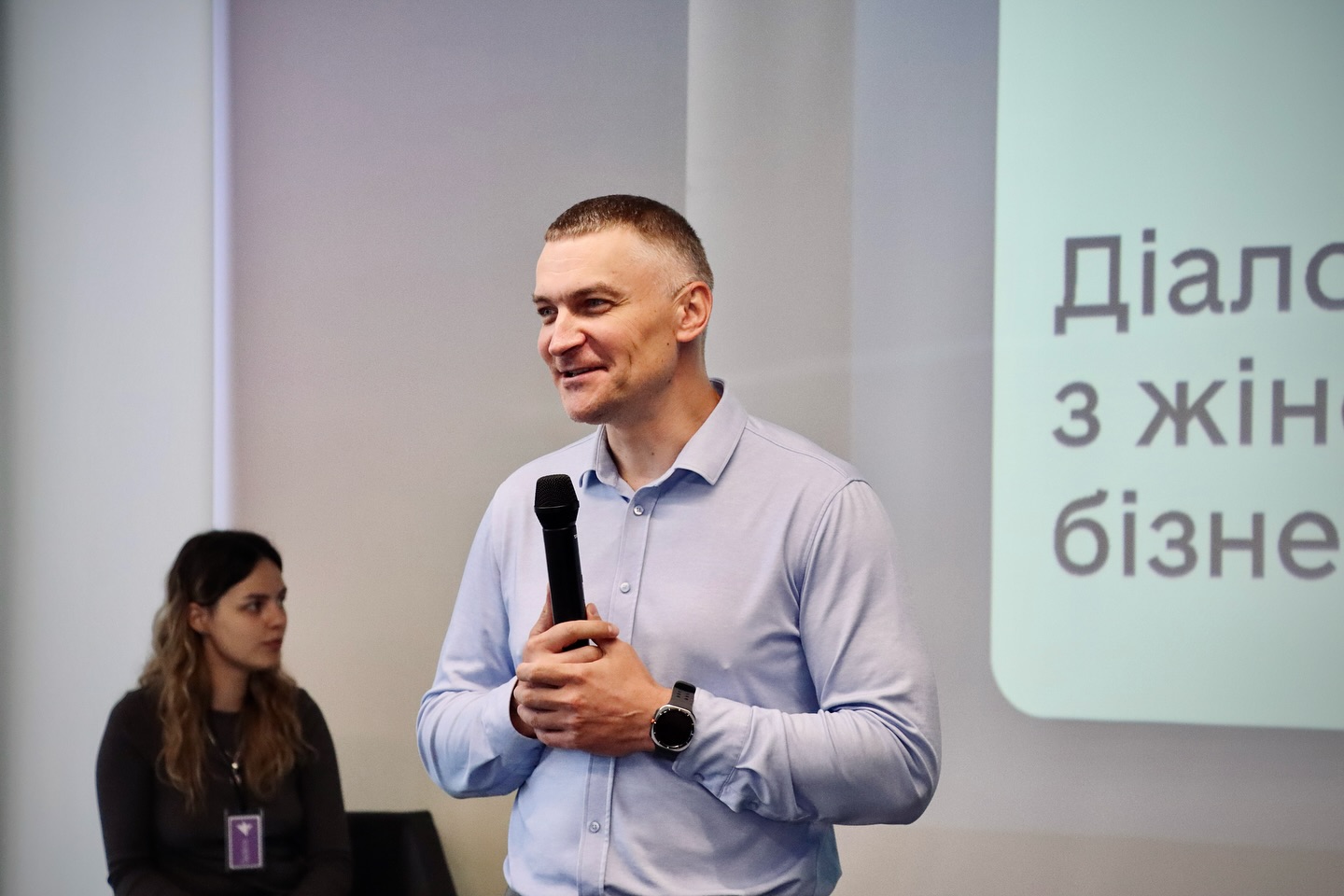 Чоловік розповідає щось в мікрофон, на задньому фоні - презентація.