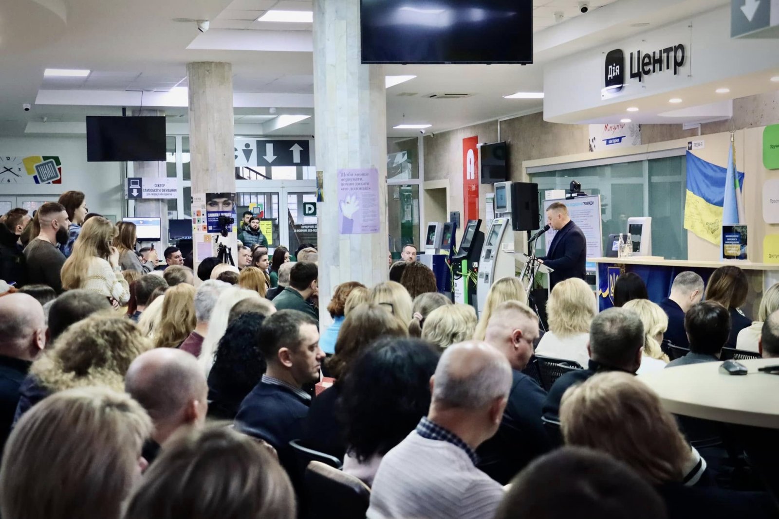 Люди сидять в приміщенні ЦНАПу і слухають доповідь.