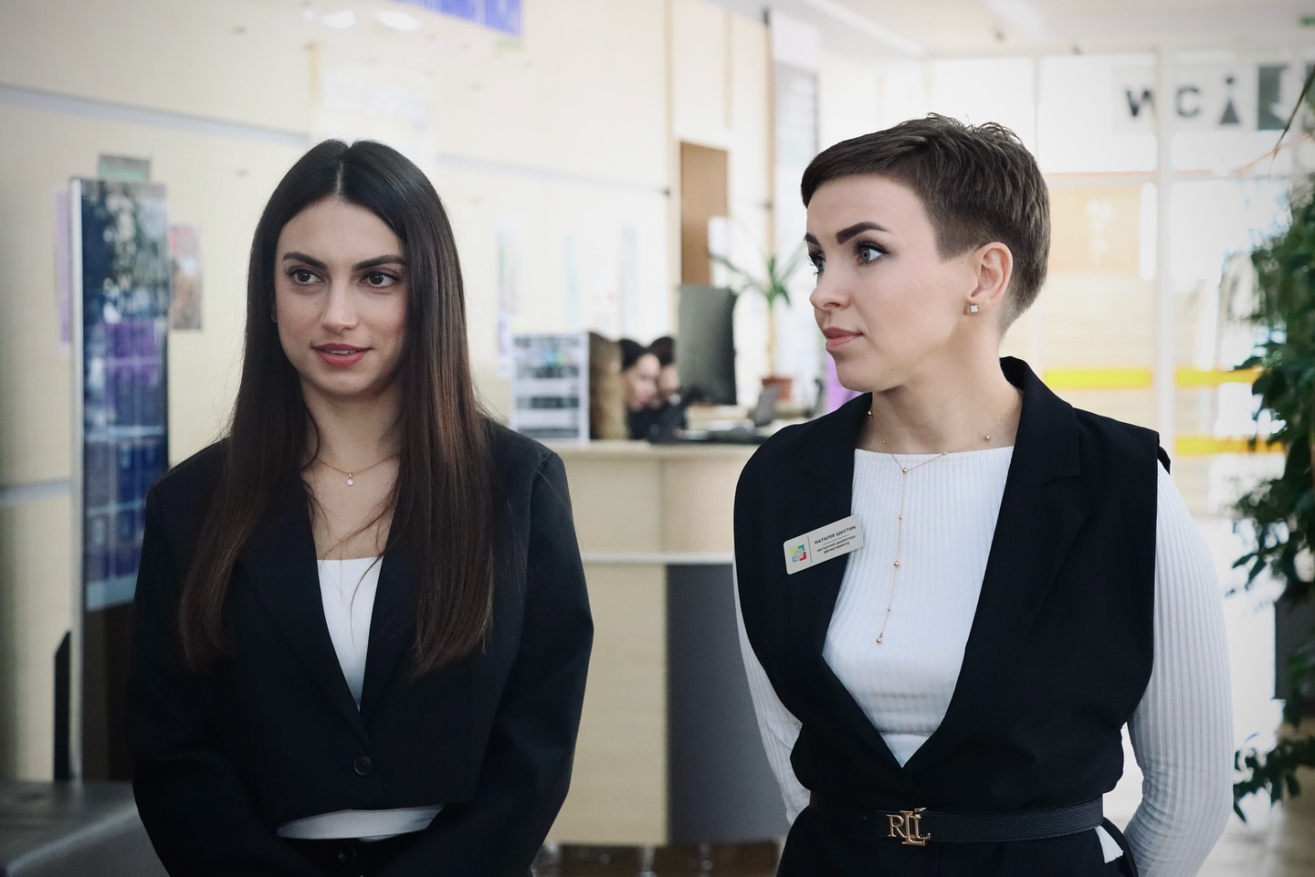 Дві жінки у діловому одязі перебувають у приміщенні.