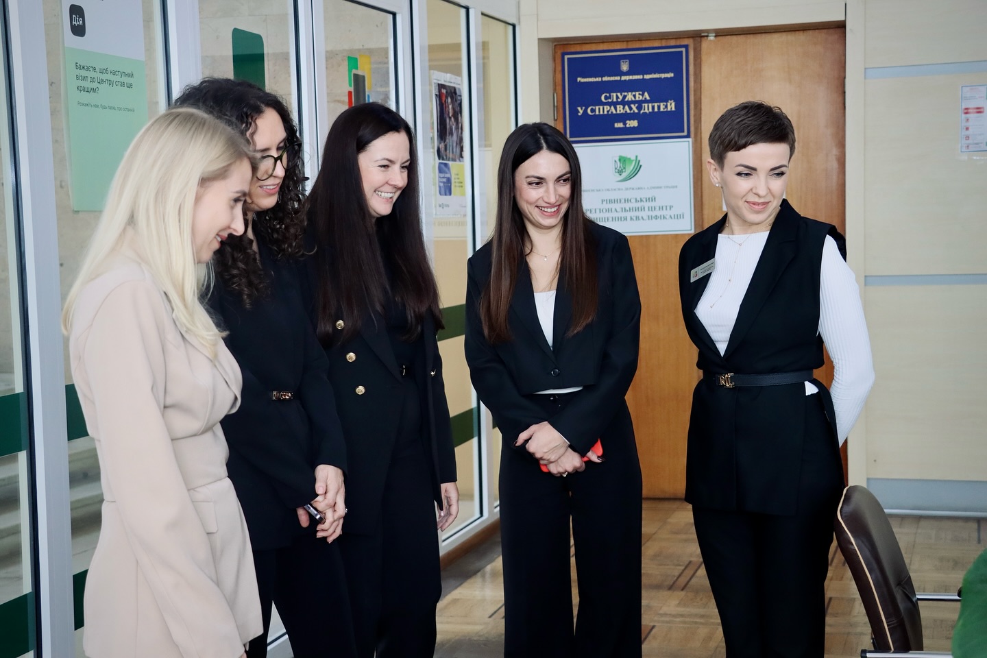 П'ять жінок стоять у приміщенні та посміхаються.