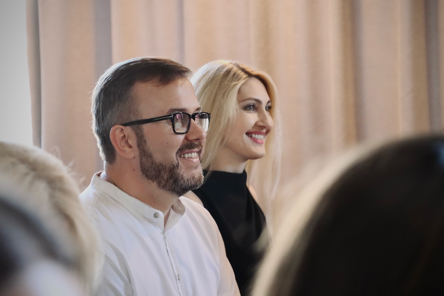 Чоловік в окулярах та жінка зі світлим волоссям сидять у приміщенні.