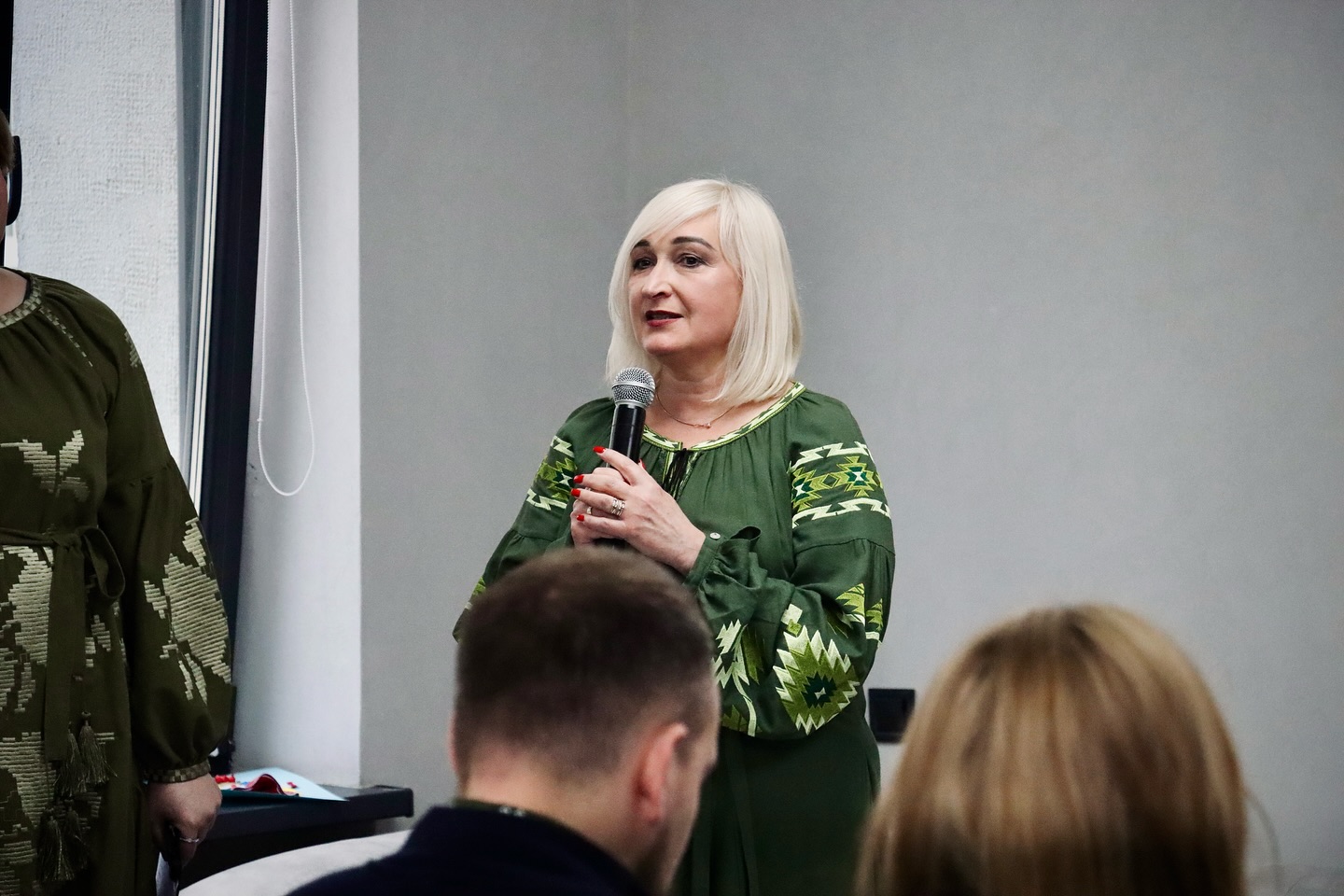 Жінка у вишитій сукні тримає мікрофон у руках.