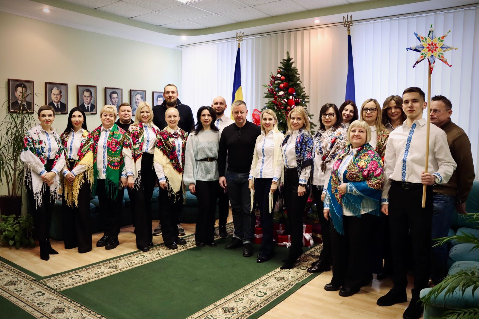 Люди у вишитих сорочках та з українськими хустками позують у приміщенні, на фоні ялинки.