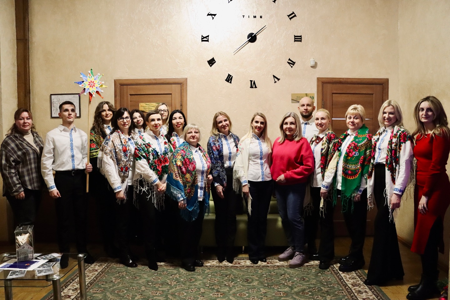 Люди позують для фото, на фоні - великий настінний годинник.