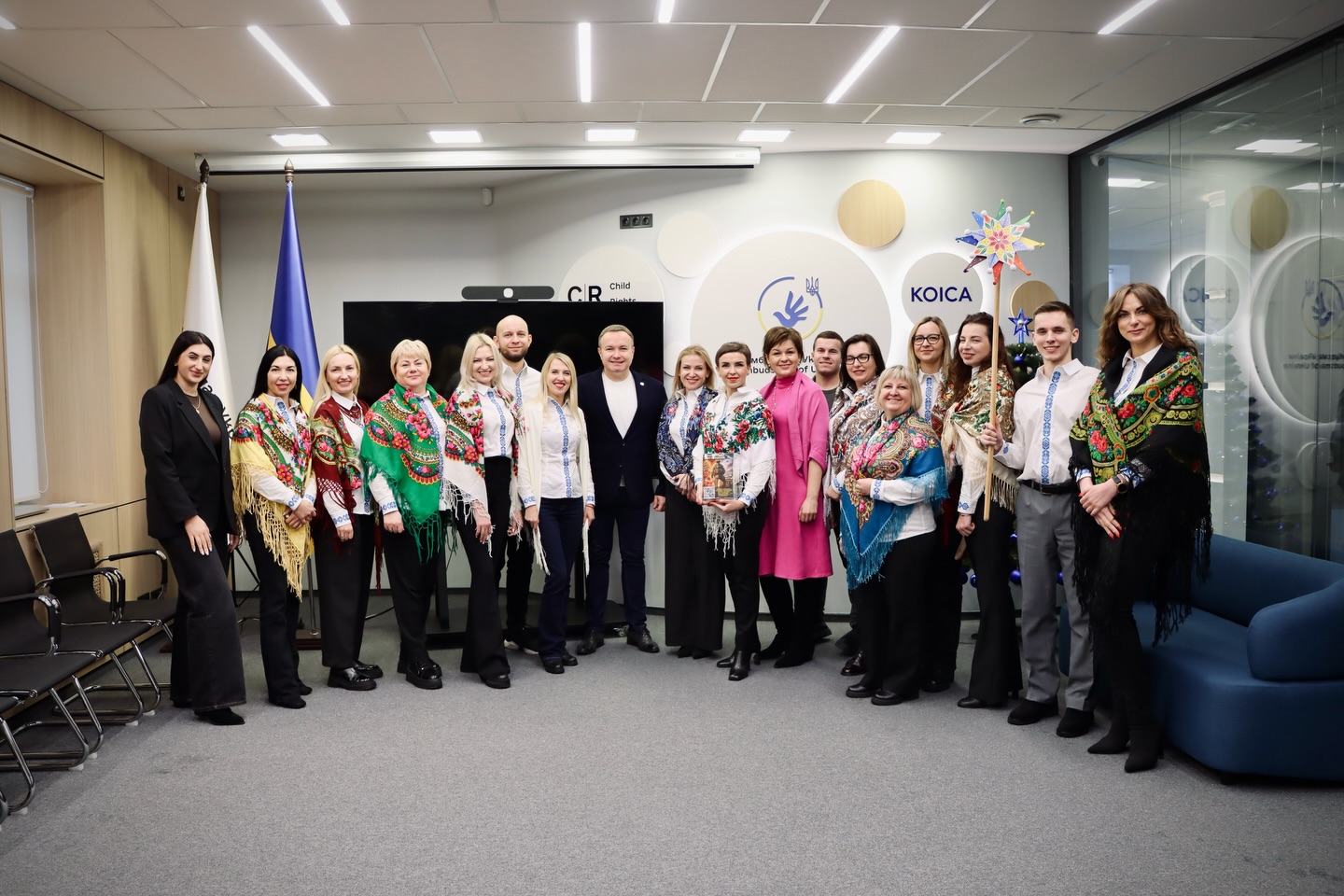 Група людей у вишитих сорочках позує для фото у приміщенні.