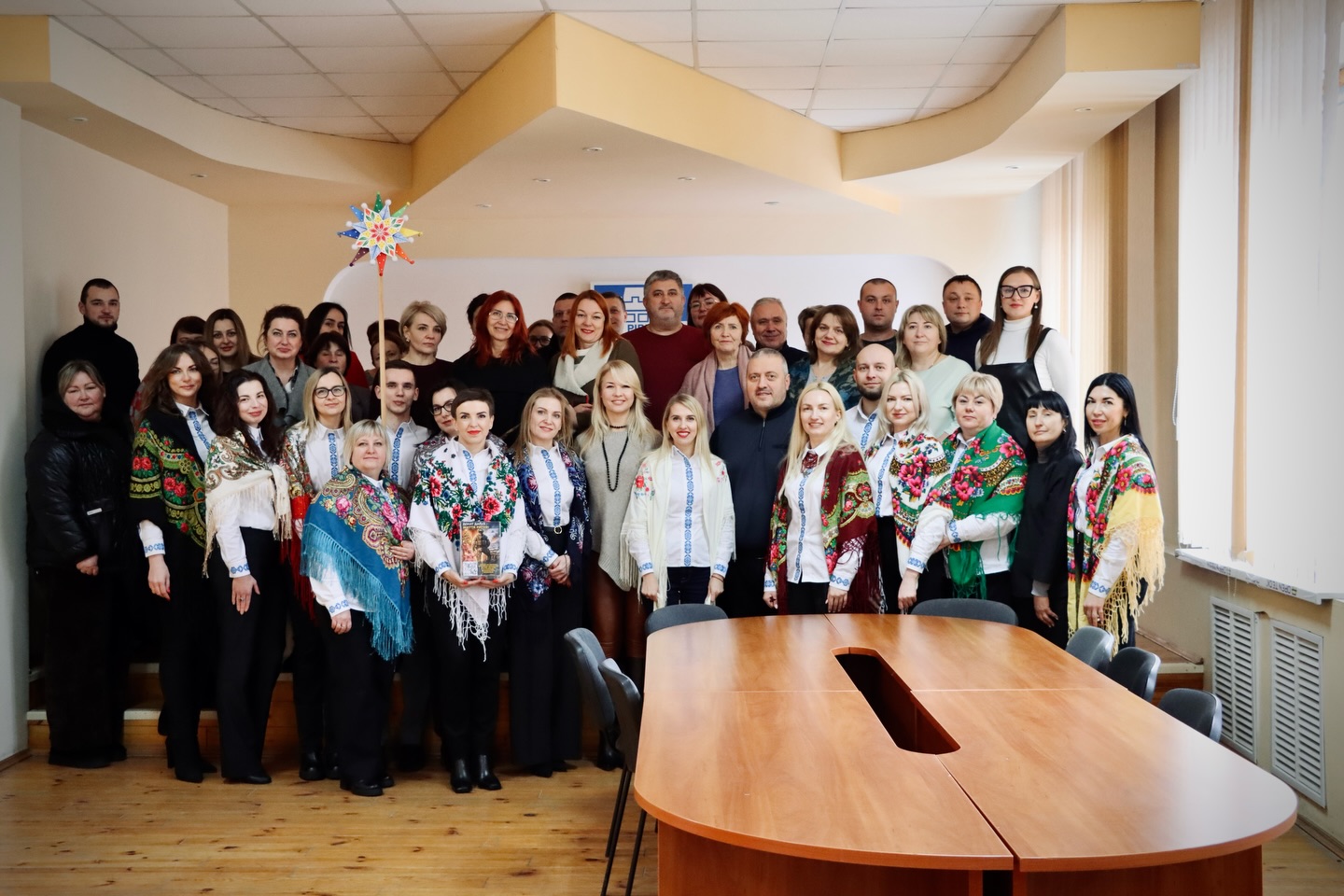 Група людей у вишитих сорочках перебувають у приміщенні.