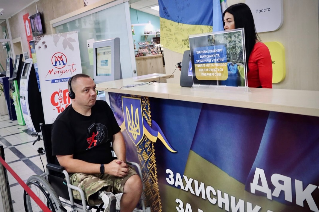Біля стійки сидить чоловік у візку, поруч стоїть жінка.