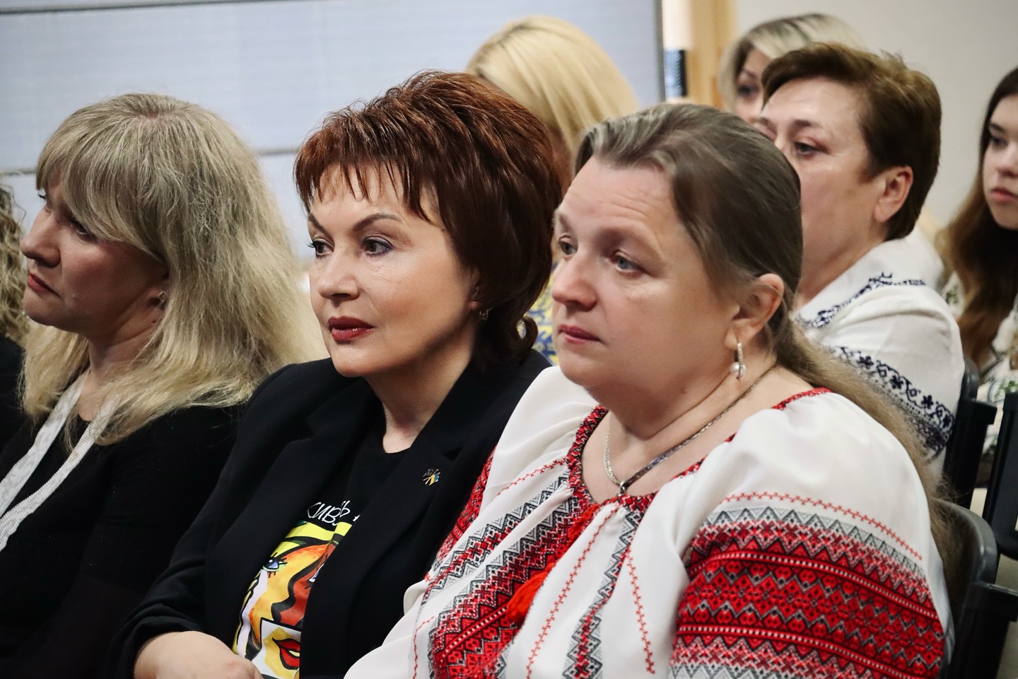 Жінки у вишитих сорочках сидять у залі.