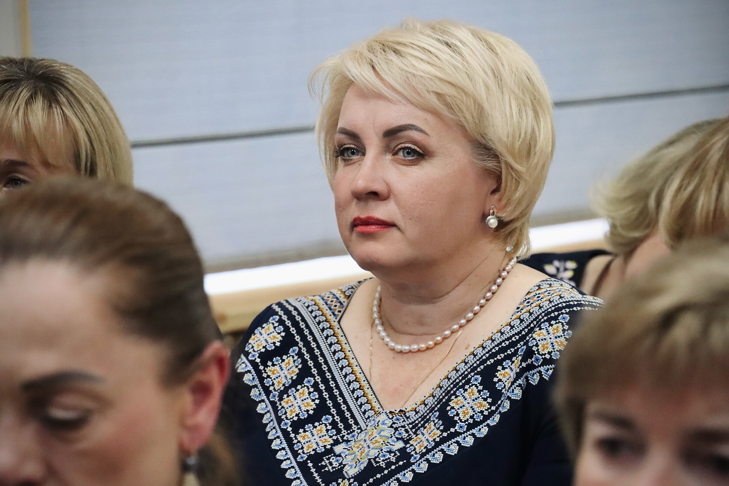 Жінка зі світлим коротким волоссям та у вишиванці сидить у залі.