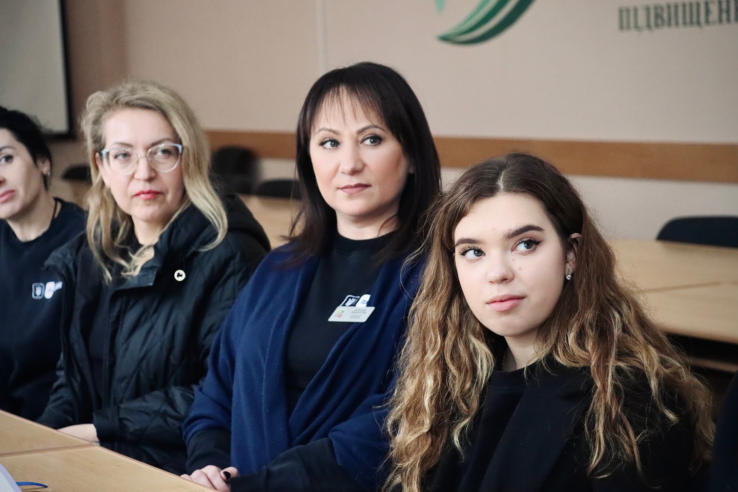 Група жінок сидять за столом та дивляться убік.