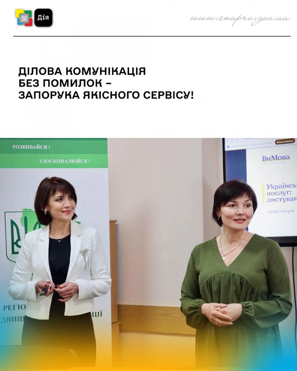 Дві жінки стоять перед банером. Одна одягнена в зелену сукню, а інша - у чорну сукню та білий жакет.