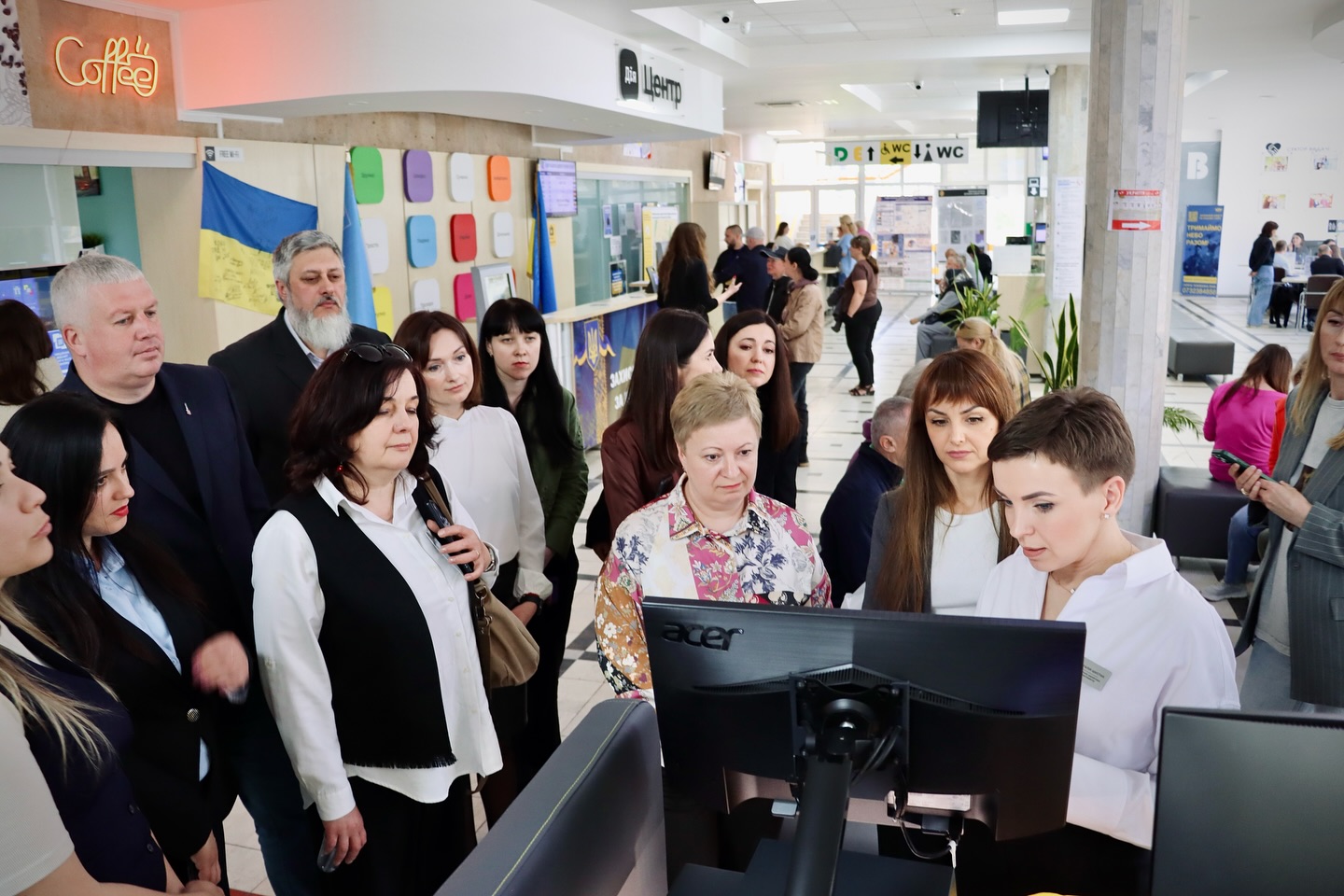 Група людей перебувають біля комп'ютера, у приміщенні.