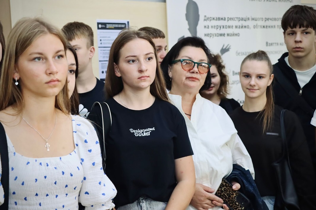 Група людей перебуває у приміщенні, позаду інформаційні стенди.