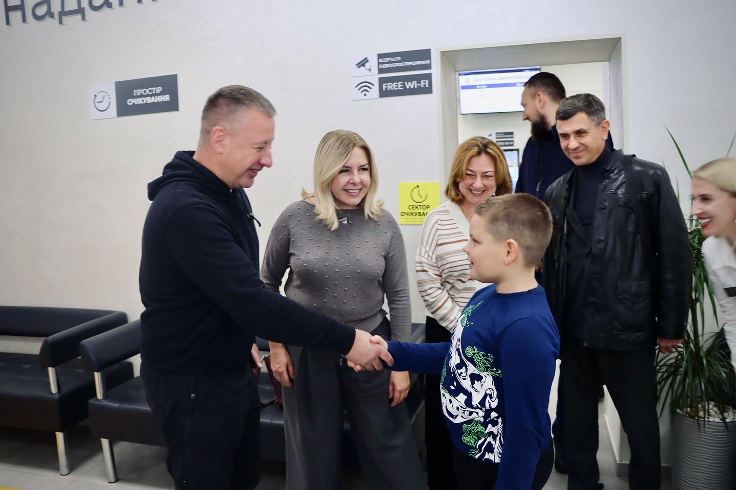 Чоловік тисне руку хлопчику, поруч кілька усміхнених людей у приміщенні