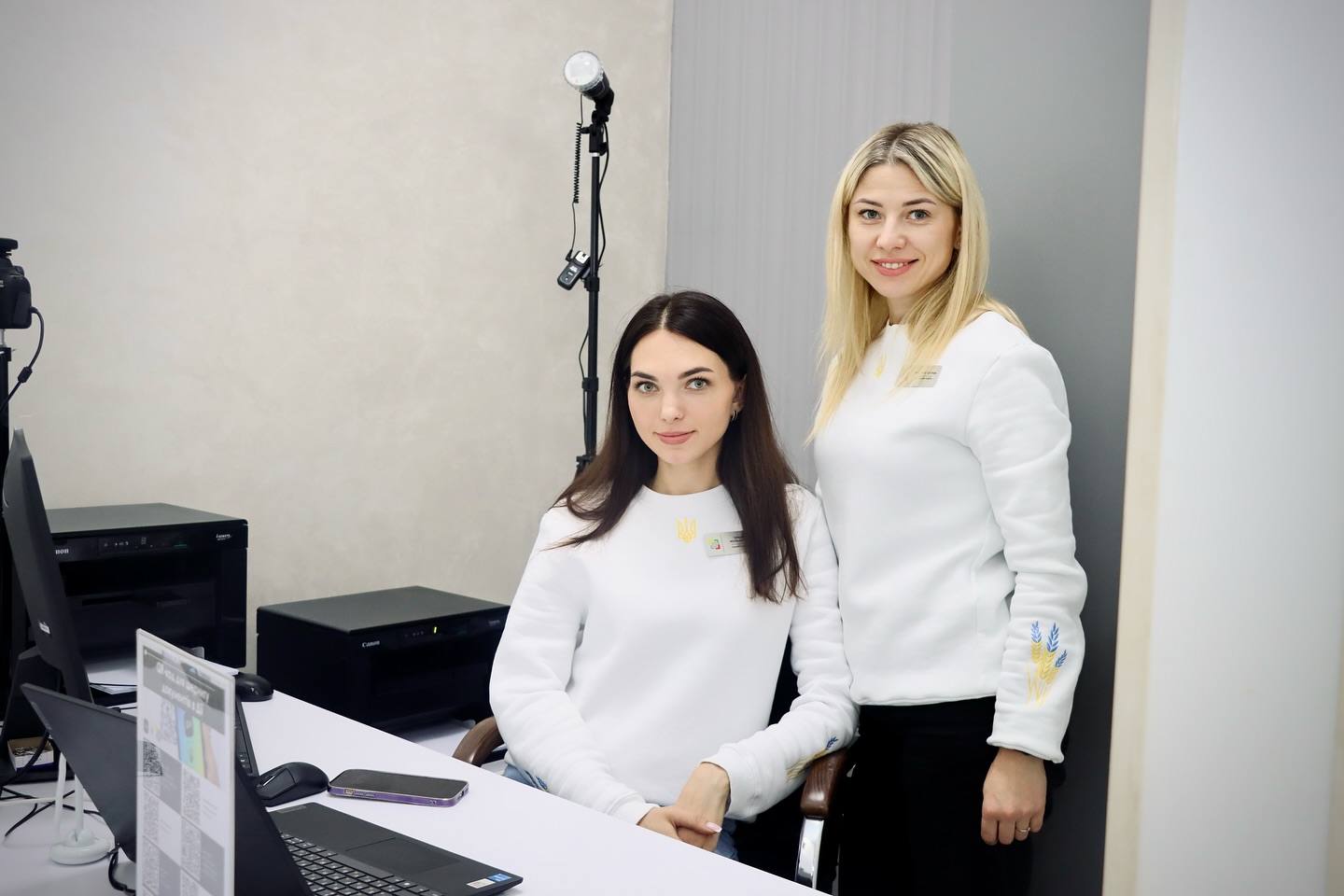 Дві жінки у білих светрах із символікою України біля робочого столу