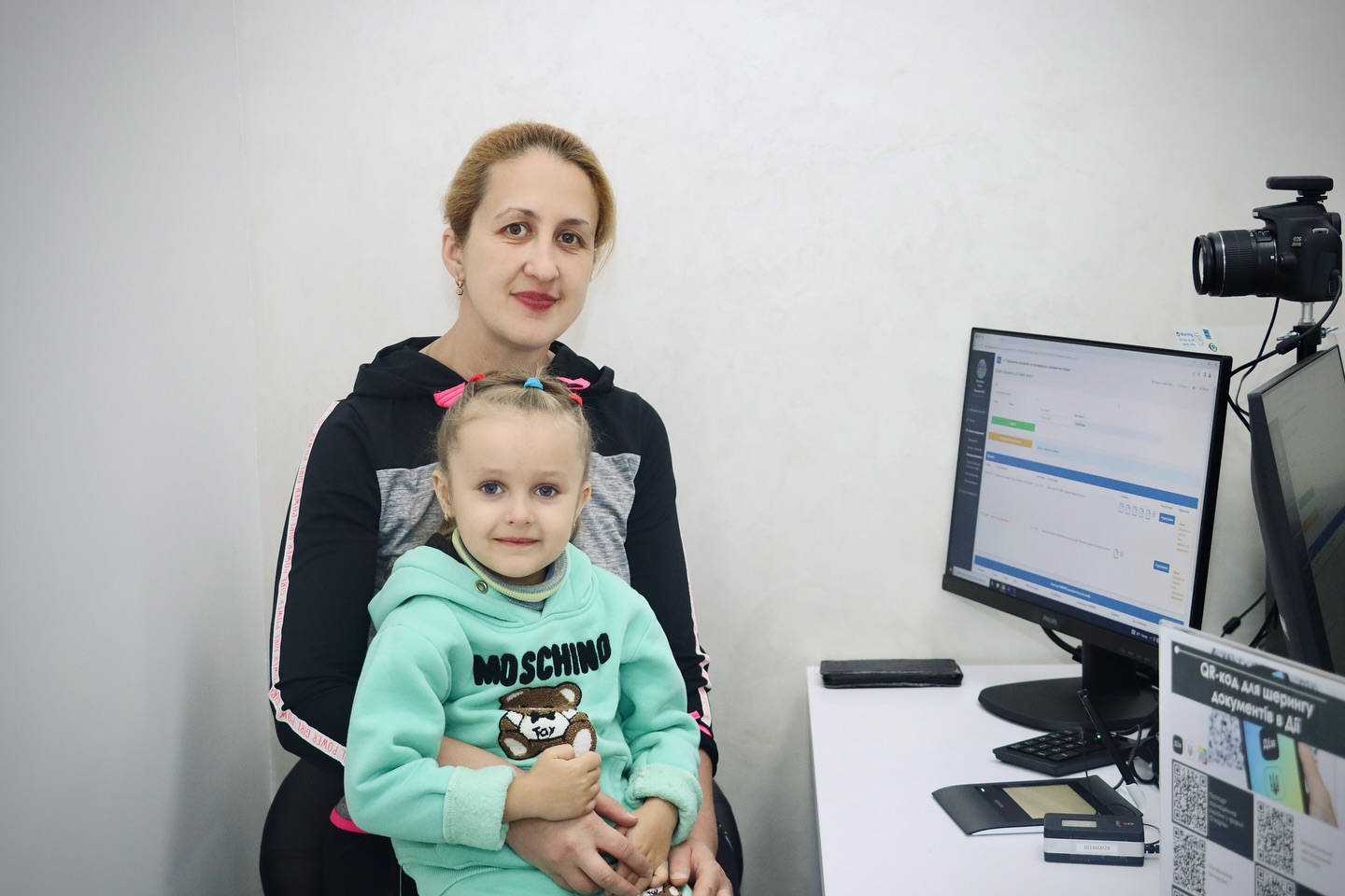 Жінка тримає дівчинку на руках, сидячі біля комп'ютера