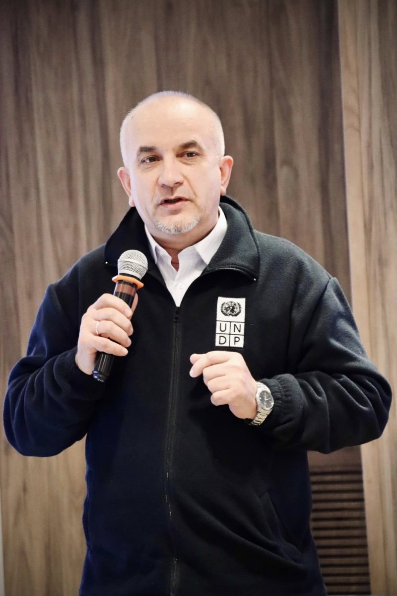 Чоловік тримає в руках мікрофон та проголошує доповідь.