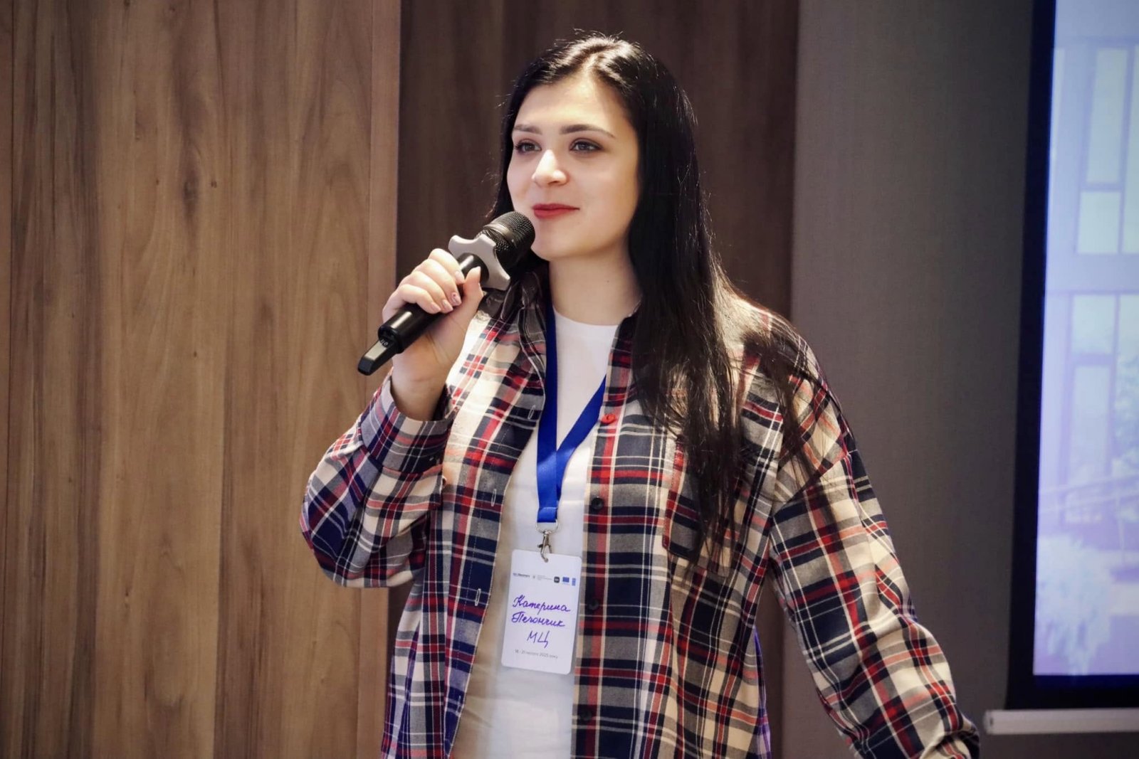 Жінка з довгим волоссям тримає в руках мікрофон та проголошує доповідь.