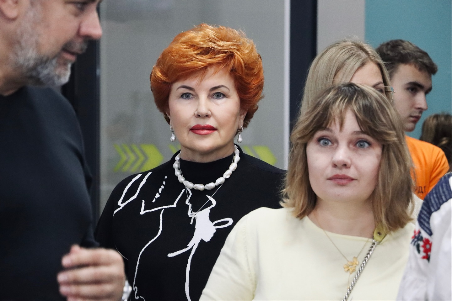 Дві жінки перебувають у приміщенні, на задньомі фоні - інші люди.