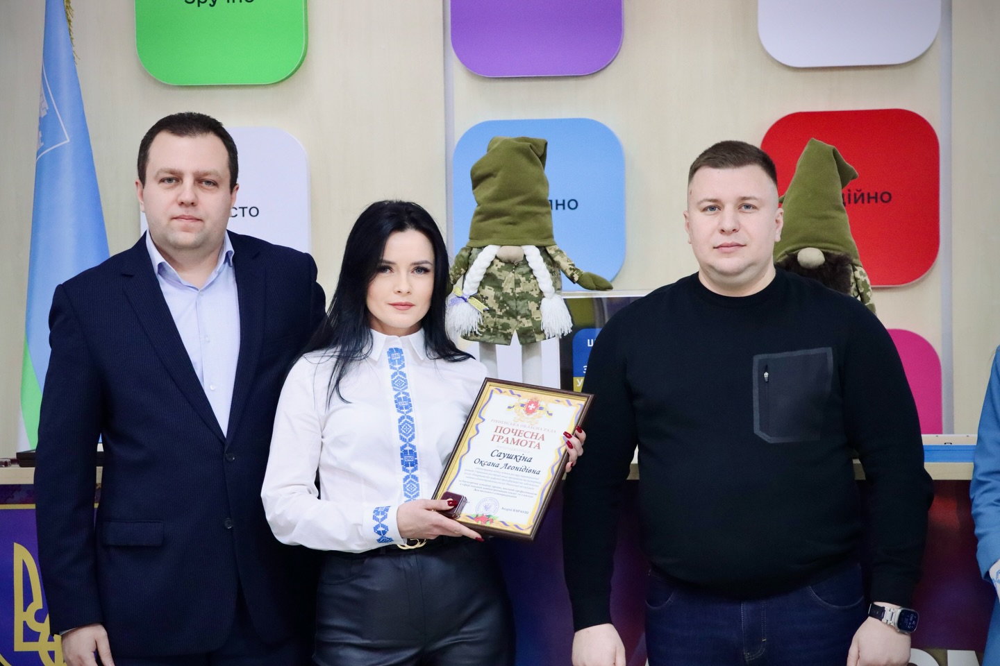 Двоє чоловіків та жінка, з темним волоссям, позують для фото з грамотою.