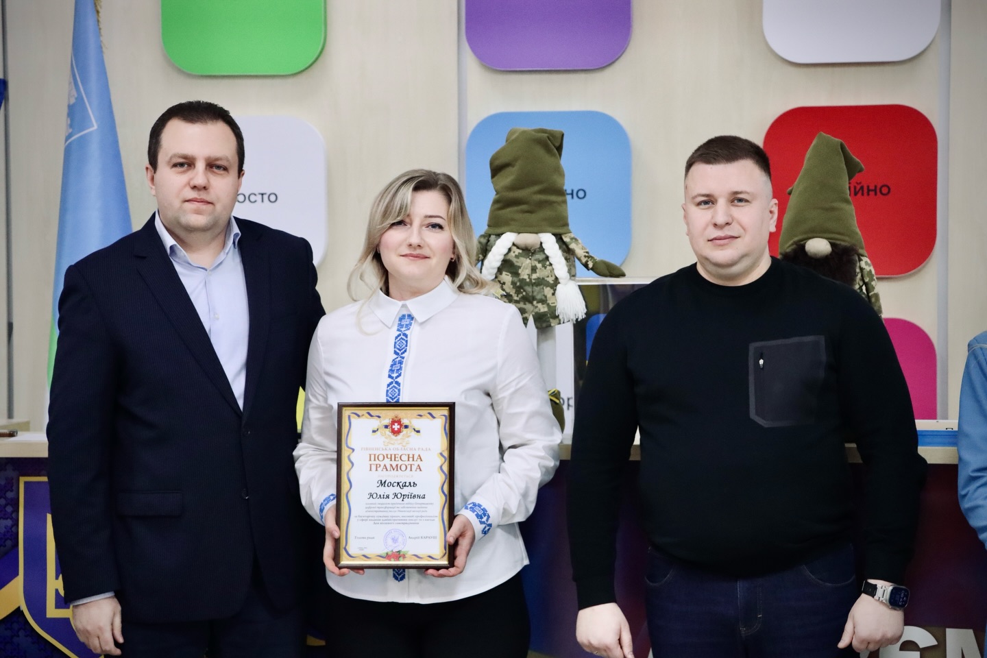 Жінка тримає подяку та стоїть між двома чоловіками.