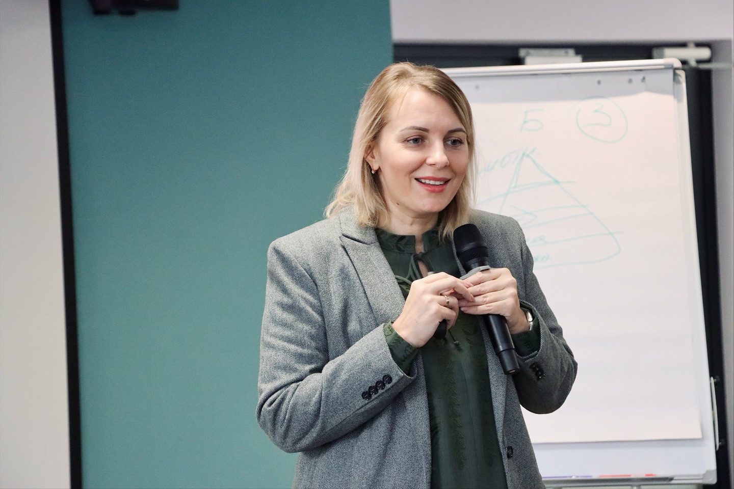 Жінка світлим волоссям тримає мікрофон у руках.