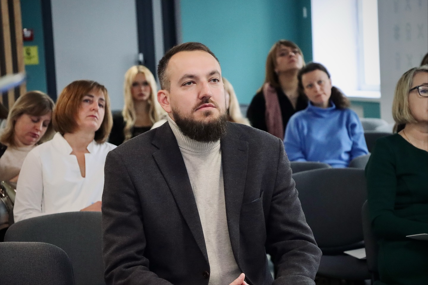 Чоловік сидить у залі, на задньому фоні - інші люди.