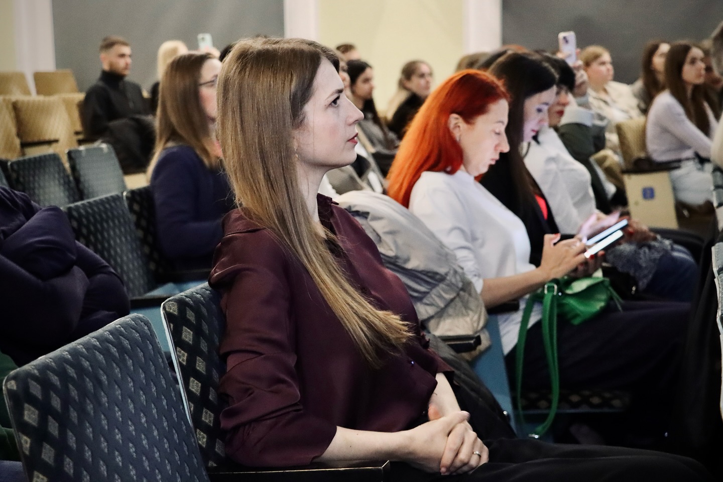 Жінка уважно слухає виступ, позаду неї інші учасниці.