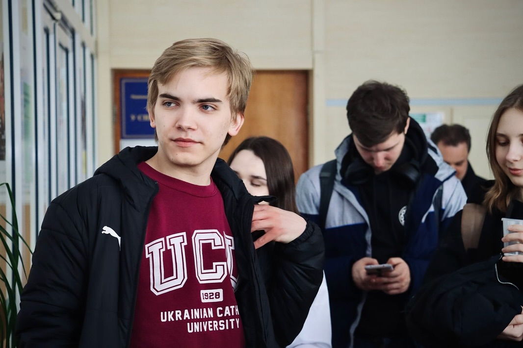 Хлопець перебуває у приміщенні. На фоні інші люди.