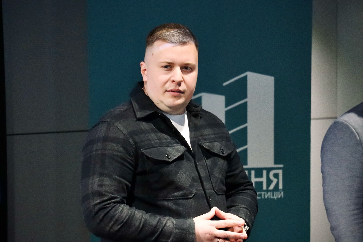 Чоловік у темному одязі стоїть у приміщенні.