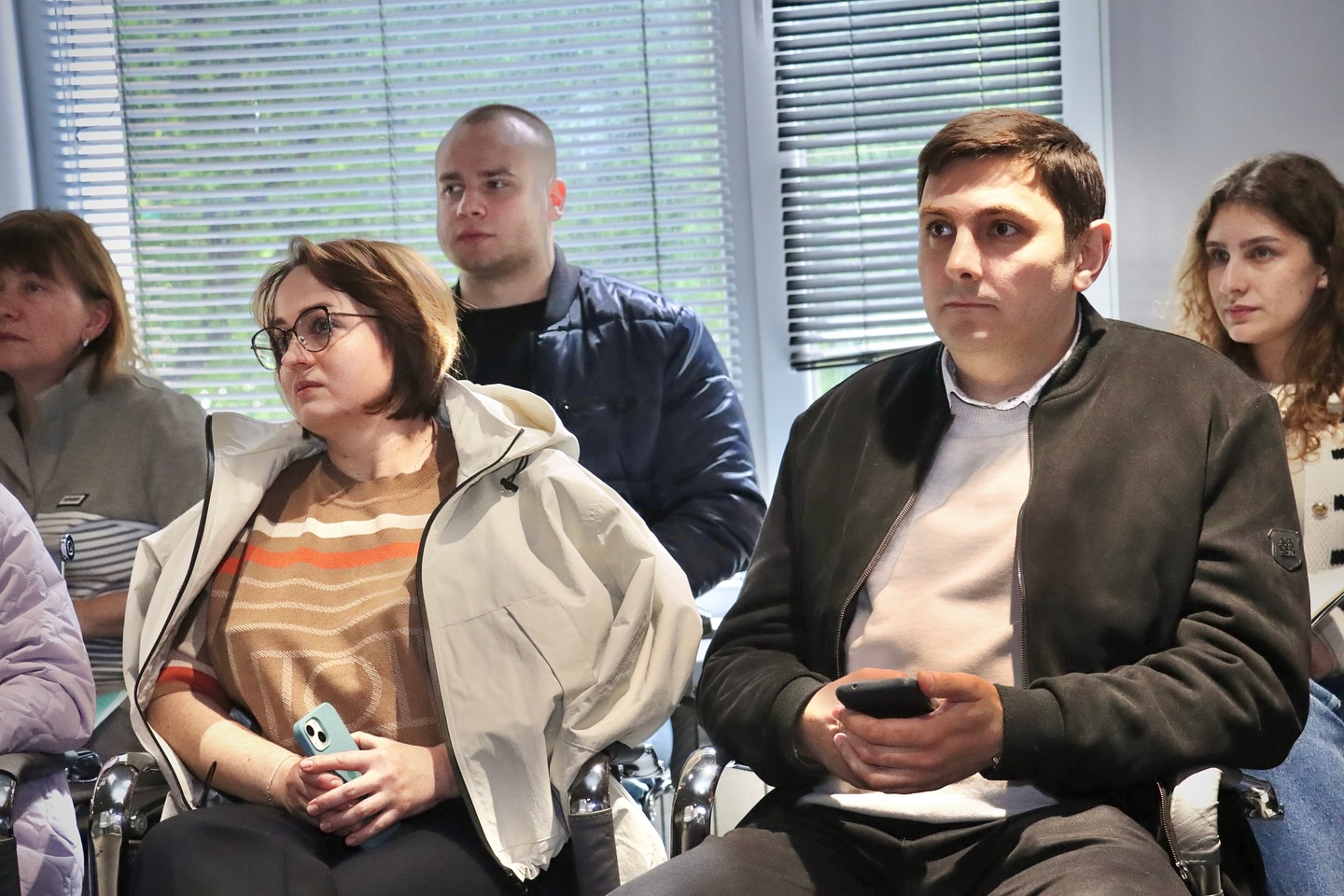 Люди сидять у приміщенні та дивляться прямо перед собою.