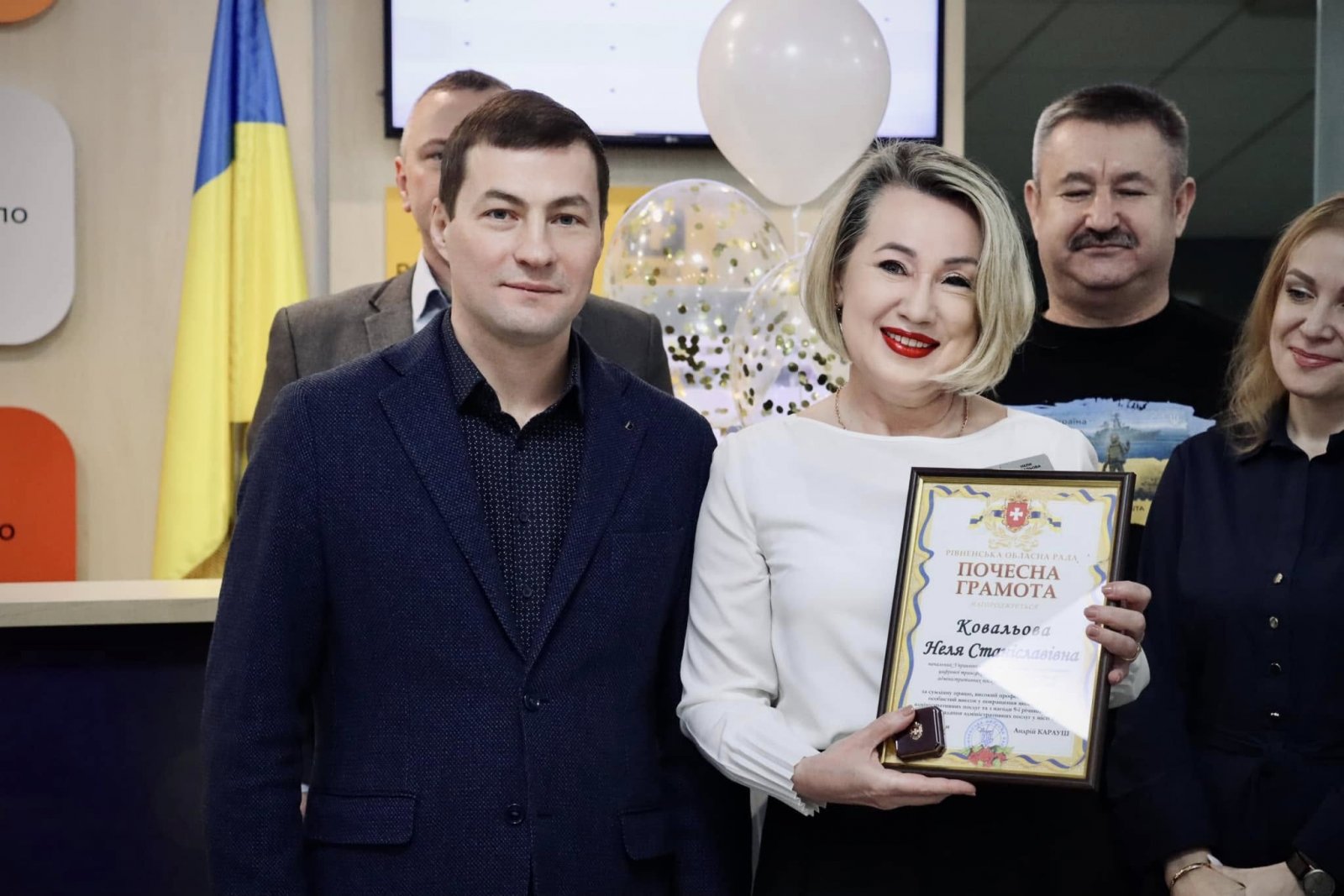 Чоловік та жінка стоять у приміщені  ЦНАПу в місті Рівному. Жінка тримає у руках грамоту.