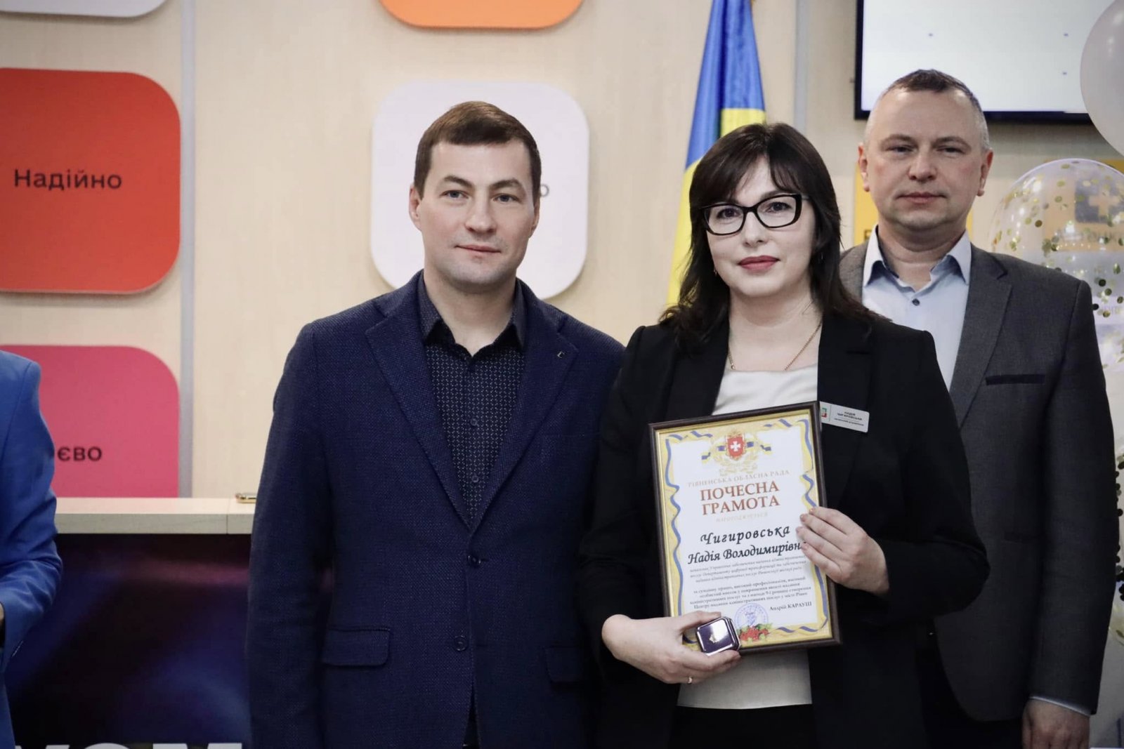 Чоловік та жінка стоять у приміщені  ЦНАПу. Жінка тримає у руках почесну грамоту.