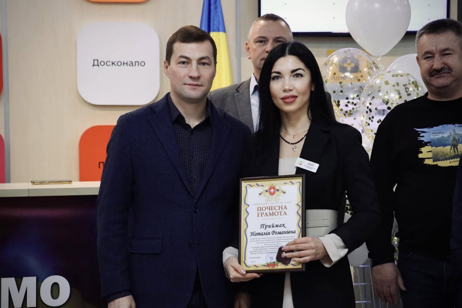 Чоловік та жінка знаходяться у приміщені  ЦНАПу в місті Рівному. Жінка тримає грамоту.