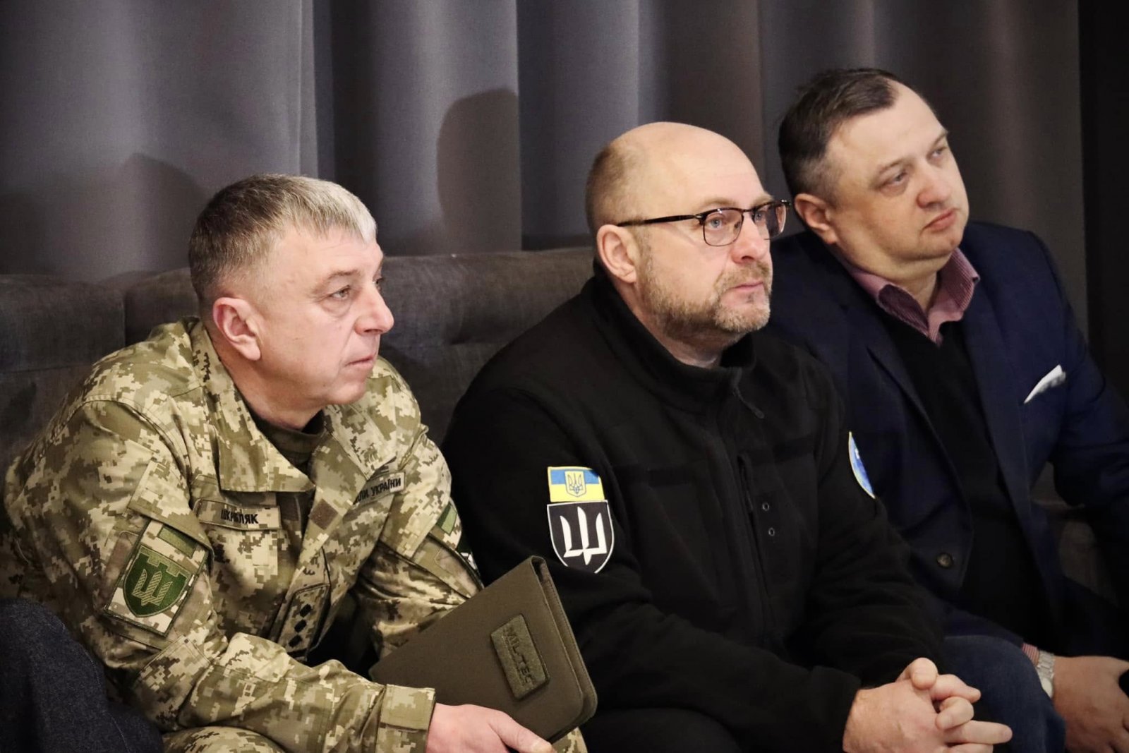 Троє чоловіків слухають доповіді на діалоговій зустрічі.