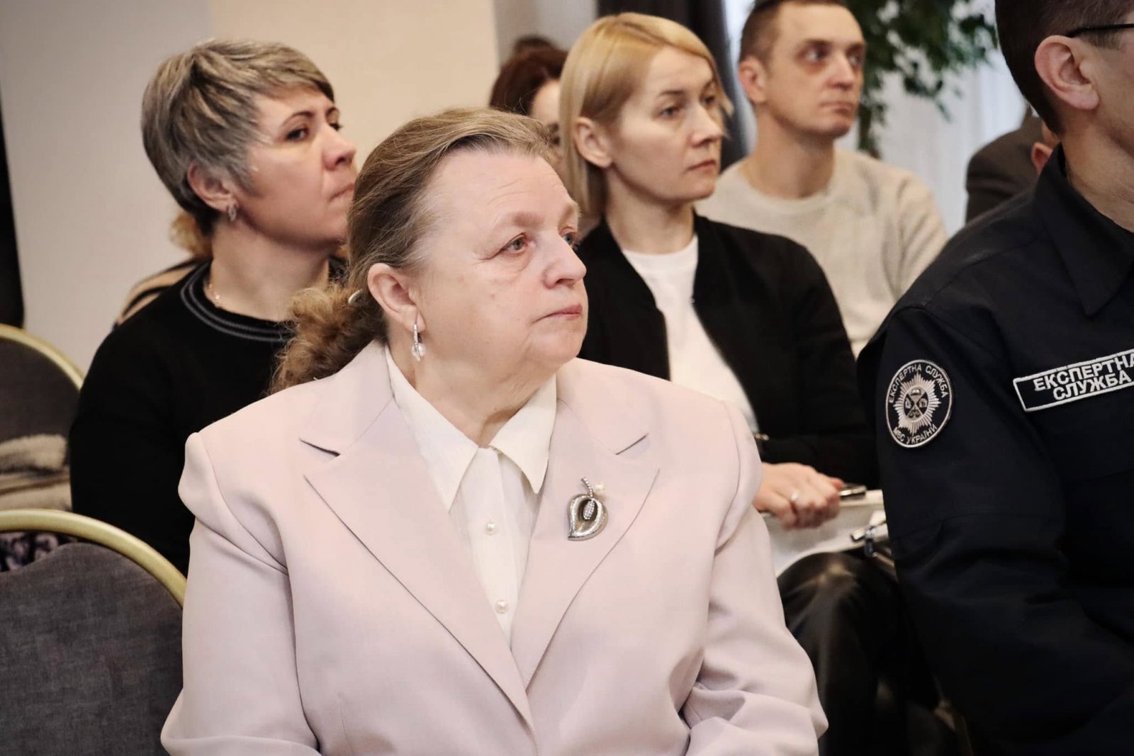 Жінка поважного віку сидить та слухає доповідь на діалоговій зустрічі.
